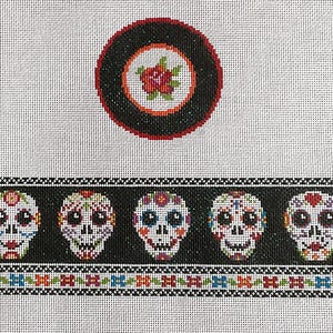 May include: Needlepoint canvas featuring a black border with five sugar skull designs. Each skull has colorful floral accents and large eyes. A circular design with a red rose is at the top.