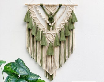 May include: A green and cream macrame wall hanging with a wooden dowel at the top. The macrame is in a geometric pattern with tassels hanging from the bottom.