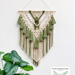 May include: A green and cream macrame wall hanging with a wooden dowel at the top. The macrame is in a geometric pattern with tassels hanging from the bottom.