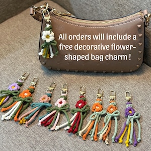 May include: A beige leather handbag with gold hardware and a series of colorful macrame flower bag charms. Each charm features a central flower, a knotted bow, and dangling cord tassels in various colors including purple, orange, pink, and red.
