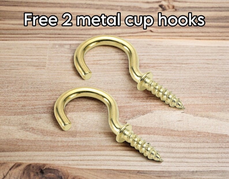 May include: Two gold-coloured metal cup hooks with screw threads, displayed on a light brown wooden surface. The text "Free 2 metal cup hooks" is at the top of the image.
