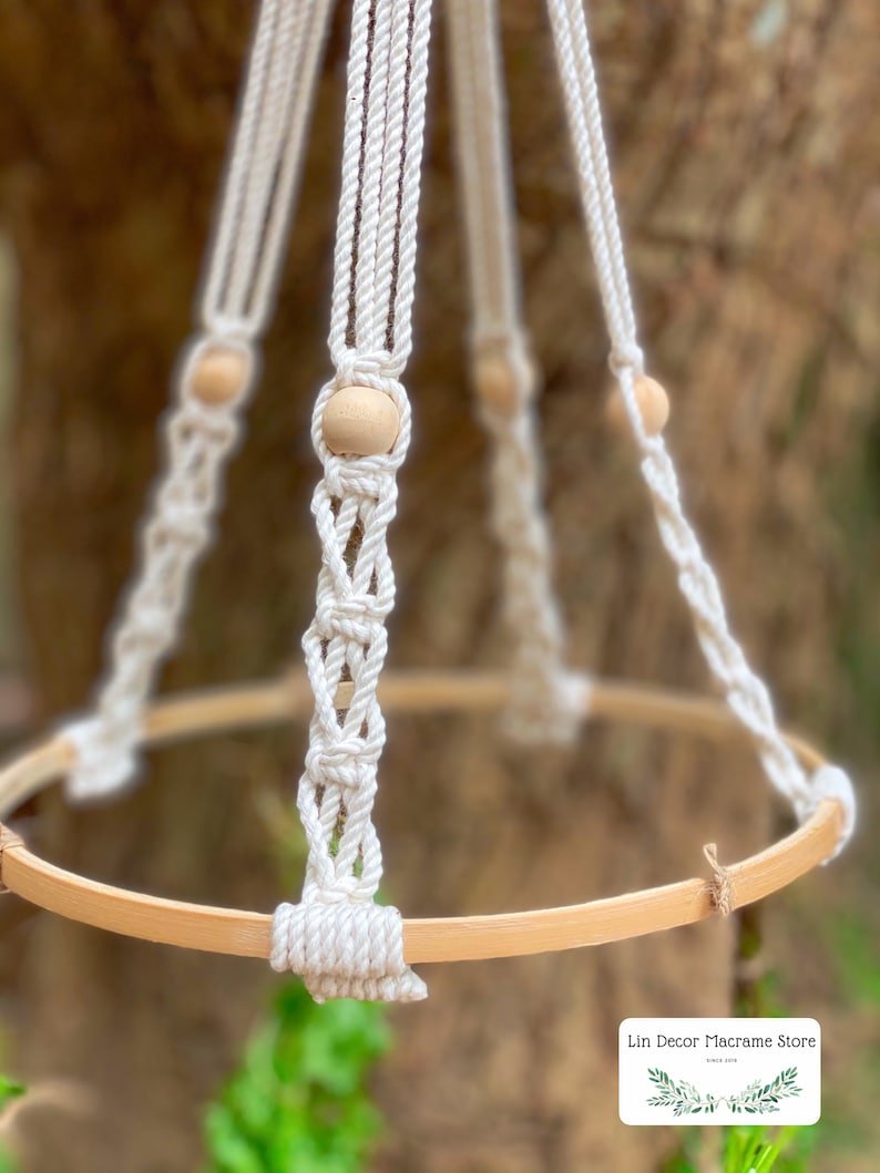 May include: A white macrame plant hanger with a wooden ring and wooden beads. The hanger is made with a thick, natural cotton rope.