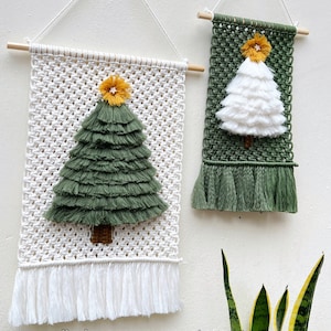 May include: Two macrame Christmas tree wall hangings. One is white with a green tree and the other is green with a white tree. Both have a yellow star on top and a wooden dowel for hanging.