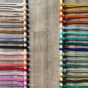 May include: A colour chart showing 32 macrame cord colours, such as cream white, yellow, and green. The colours are displayed on wooden dowels against a wood grain background. The text "32 MACRAME COLOR" is at the top, and the Etsy shop URL is at the bottom.