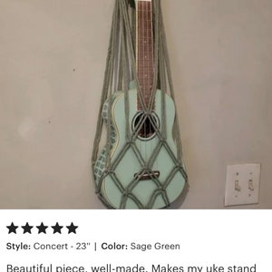 May include: Sage green ukulele hanging in a macrame wall stand. The stand is made of natural colored rope. The ukulele is a concert size, 23 inches long. "Custome Review" is written at the top of the image.