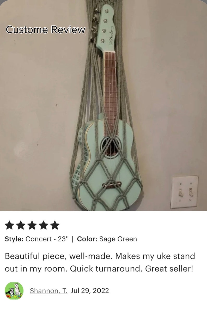May include: Sage green ukulele hanging in a macrame wall stand. The stand is made of natural colored rope. The ukulele is a concert size, 23 inches long. "Custome Review" is written at the top of the image.