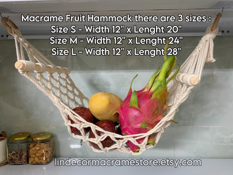 May include: A cream-coloured macrame fruit hammock, with wooden dowels, filled with fresh fruit. The hammock is suspended from the ceiling. The text on the image indicates three sizes: S (30cm x 51cm), M (30cm x 61cm), and L (30cm x 71cm).
