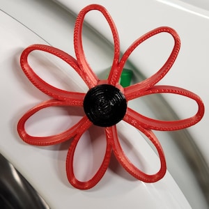 May include: A red paper flower with a black center. The flower is made of multiple layers of paper and has a textured edge.