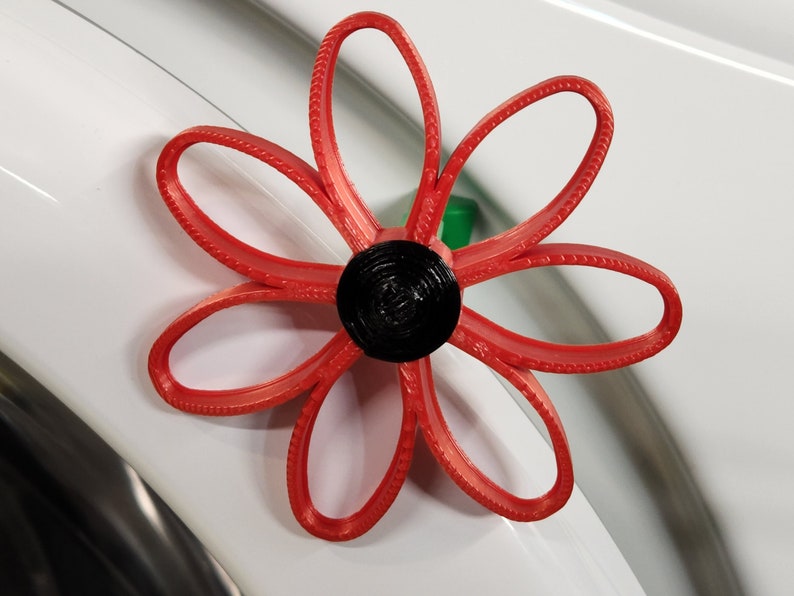 May include: A red paper flower with a black center. The flower is made of multiple layers of paper and has a textured edge.