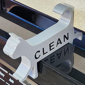 May include: A white 3D printed cat figurine with the word "CLEAN" printed on its back. The cat is standing on a black surface.