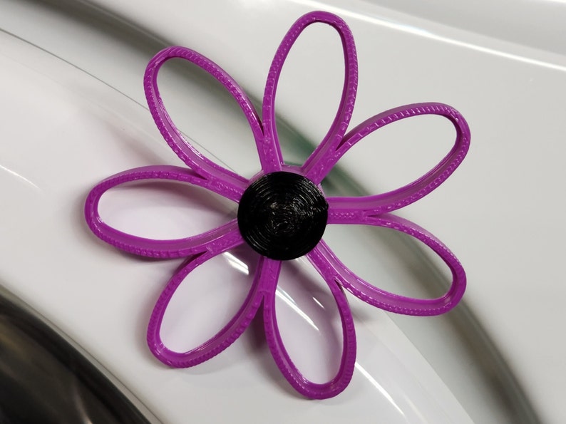 May include: A purple flower-shaped object with a black center. The flower has six petals and is made of plastic.