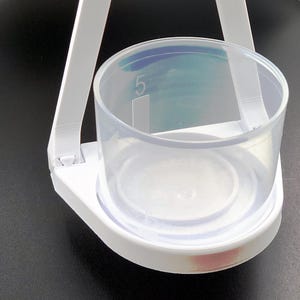 May include: White plastic measuring cup with a clear plastic bowl hanging from a white plastic frame. The bowl has a blue and green gradient and the number "5" printed on the side.