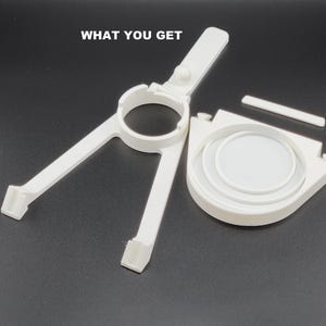 May include: White plastic 3D printed parts for a DIY project. The parts include a ring, a base with a handle, and a flat piece.