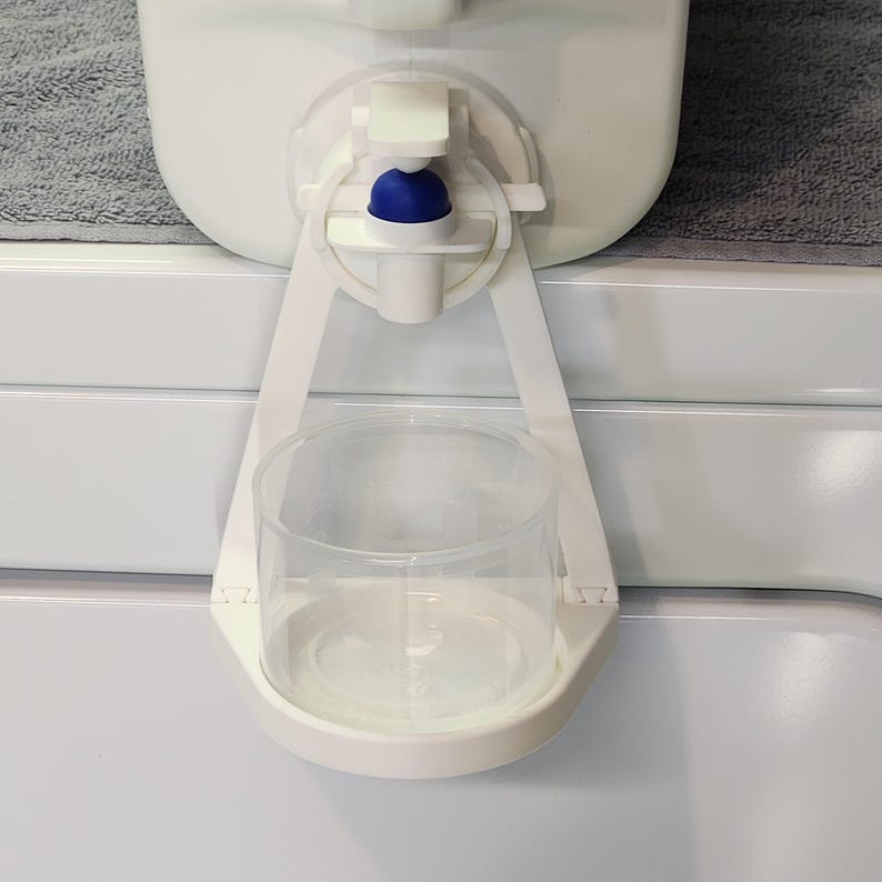 May include: White plastic water dispenser with a blue spout and a clear glass cup holder.