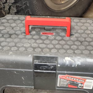 May include: Black plastic toolbox with a red handle and a black latch. The toolbox has a textured surface and a label that says "Rubbermaid".