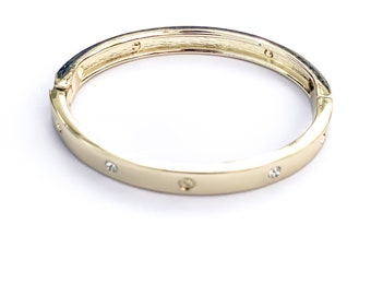 Puede incluir: Brazalete rígido dorado con pequeños detalles de cristal transparente. El brazalete tiene un acabado liso y pulido y un diseño sencillo y elegante. El brazalete tiene aproximadamente 6,35 cm de diámetro.