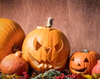 Puede incluir: Tres calabazas talladas, una con una cara de miedo, otra con una cara sonriente y otra con un diseño simple. Las calabazas están rodeadas de hojas de otoño y bayas rojas.