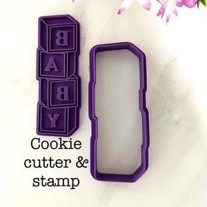 Op de afbeelding: Een paarse koekjessnijder en stempelset. De stempel vormt het woord "BABY" in gestapelde blokletters. De koekjessnijder heeft een rechthoekige vorm. De tekst "Cookie cutter & stamp" staat eronder.