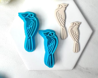May include: Four cookie cutters in the shape of birds. Two are blue and two are beige. The blue cutters are layered to create a 3D effect.