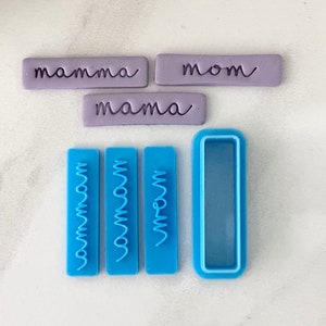 May include: A set of four blue plastic cookie cutters with the word "mom" in a cursive font. There are three cutters with the word "mom" in a vertical orientation and one cutter with a rectangular shape.