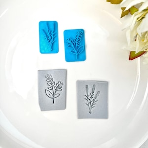 May include: Four different silicone stamps for baking and crafting. Two stamps are blue and feature a sprig of leaves. Two stamps are gray and feature a sprig of leaves and a sprig of lavender.