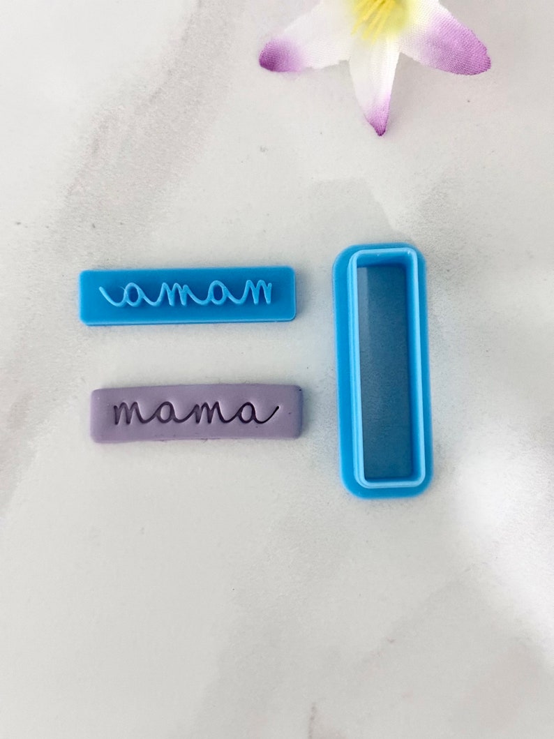 May include: Two blue plastic cookie cutters, one with the word "mama" and the other a rectangle. A purple fondant cutout with the word "mama" is also shown.