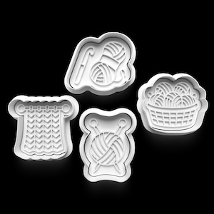 May include: Four white plastic cookie cutters in the shape of knitting and crochet tools. The shapes include a ball of yarn with a crochet hook, a basket of yarn balls, a knitted piece, and a ball of yarn with knitting needles.