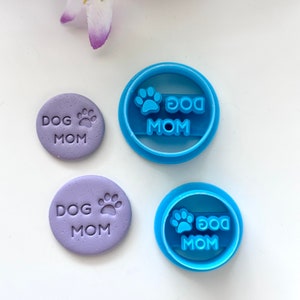 May include: Two blue plastic cookie cutters and two purple fondant impressions with the text "Dog Mom" and a paw print.