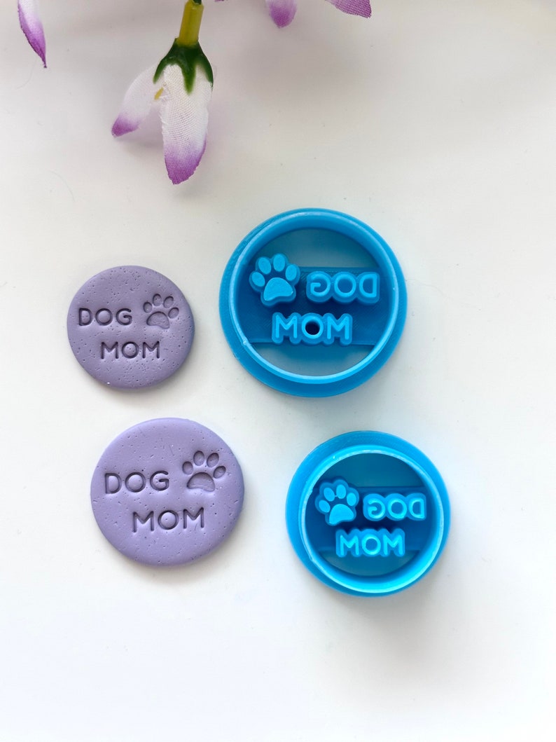 May include: Two blue plastic cookie cutters and two purple fondant impressions with the text "Dog Mom" and a paw print.