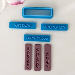 May include: A set of six blue and purple polymer clay stamps with different spellings of the word "mom". The stamps are rectangular and have a raised design. The words on the stamps are "mom", "mama", "mamma", "mom", "mommy", and "mom".