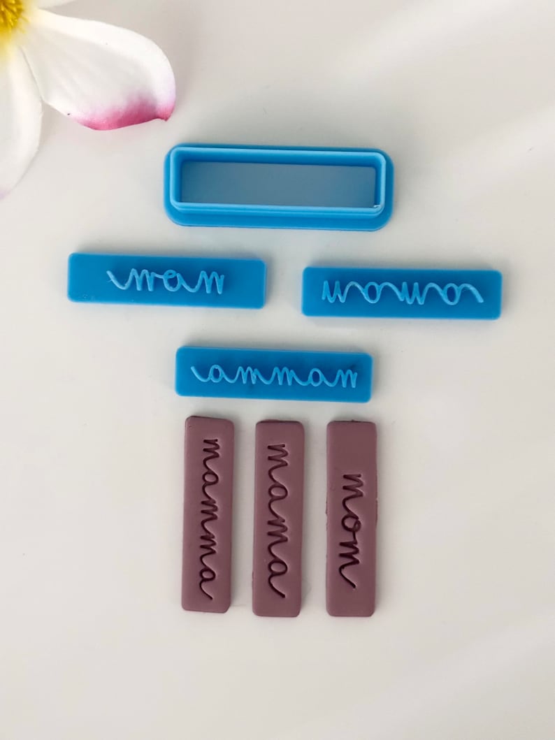 May include: A set of six blue and purple polymer clay stamps with different spellings of the word "mom". The stamps are rectangular and have a raised design. The words on the stamps are "mom", "mama", "mamma", "mom", "mommy", and "mom".