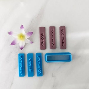 May include: A set of nine blue and purple polymer clay stamps with the words "mom", "mamma", "mama", "mommy", "momma", and "mommy" in a cursive font. The stamps are arranged on a white marble surface.