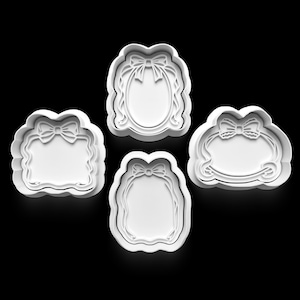 May include: Four white cookie cutters in various shapes, including oval and rectangular frames, each adorned with a bow at the top. The cutters have a scalloped edge and are set against a black background.