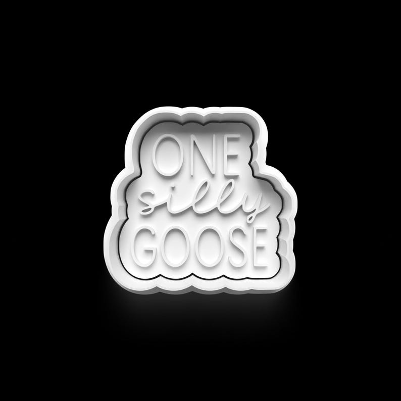 May include: A white cookie cutter in the shape of a cloud with the words "ONE silly GOOSE" in a whimsical font. The cookie cutter is set against a black background.