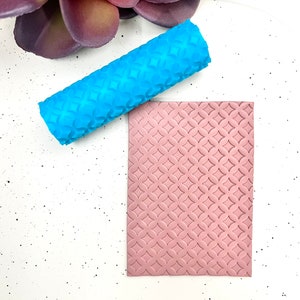 May include: A blue and pink silicone rolling pin and a silicone mat with a repeating geometric pattern. Both tools are used for creating embossed designs in clay or fondant.