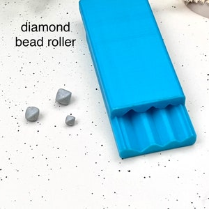 May include: A blue plastic bead roller with a diamond pattern. Three small, silver-colored beads are on a white surface.