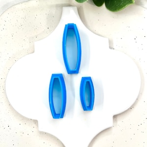 May include: Three blue plastic cookie cutters shaped like ovals, arranged in descending size order on a white background.