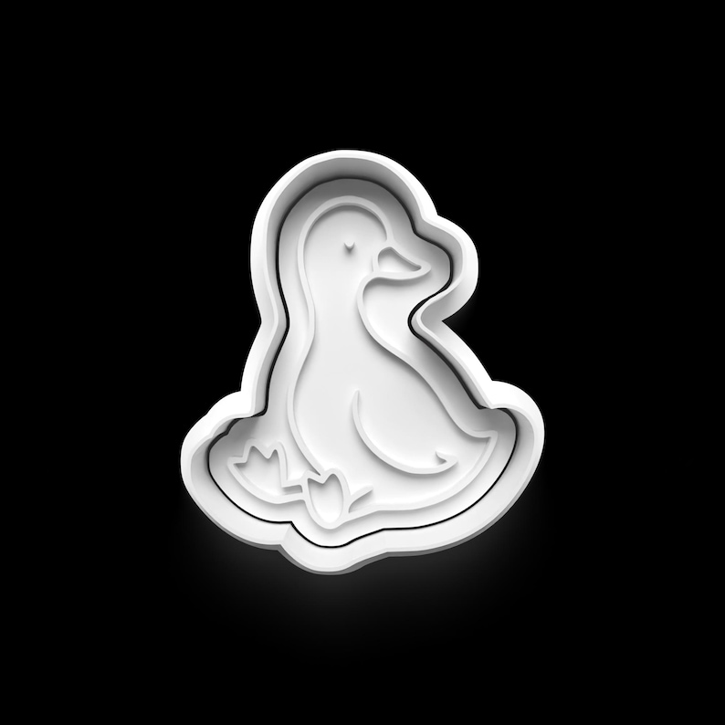 May include: A white plastic cookie cutter in the shape of a duckling, with detailed lines defining the body, wings, and feet. The duckling is sitting down. The cutter is on a black background.