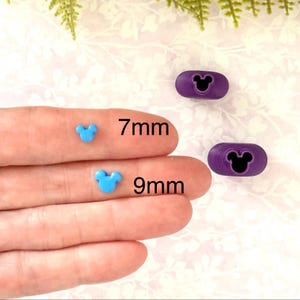 May include: The image displays two blue Mickey Mouse-shaped beads, 7mm and 9mm in size, and two purple oval-shaped beads with a Mickey Mouse silhouette. The beads are likely for crafting or jewelry making.