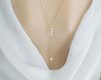 May include: A delicate gold-tone necklace with a Y-shaped design. The necklace features three small, round pearls cascading down the front, with a single pearl at the end of the drop. The necklace is worn against a white fabric.