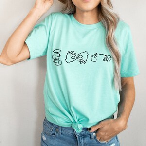 May include: A turquoise t-shirt with a graphic of the word "love" spelled out in American Sign Language.