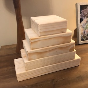 May include: A set of five wooden risers, stacked in a pyramid shape. The risers are made of natural, unpainted wood and have a smooth, polished finish.