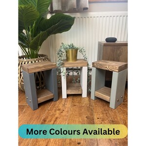 May include: Three wooden side tables with two shelves each. The tables are painted in different colours: grey, white, and green. The tables are on a wooden floor. "More Colours Available" is written on the bottom of the image.