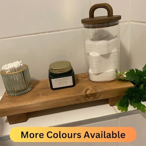 May include: A rectangular wooden riser with four small feet, holding a fluted glass jar filled with cotton swabs, a small dark green jar labelled Eucalyptus, and a tall glass canister with a wooden lid containing white cotton pads.