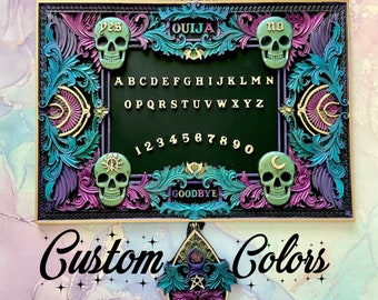 Puede incluir: Un tablero de Ouija enmarcado en negro con una superficie de fieltro verde y detalles dorados. El tablero presenta un alfabeto tradicional, números y las palabras "sí", "no" y "adiós". El tablero está rodeado por un marco decorativo con calaveras y diseños florales en tonos morados, verde azulado y dorado.