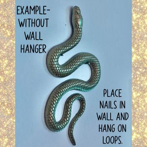 May include: A gold-colored snake sculpture with a textured surface. The sculpture is hanging from two loops. The text "EXAMPLE-WITHOUT WALL HANGER" is written above the sculpture. The text "PLACE NAILS IN WALL AND HANG ON LOOPS." is written below the sculpture.
