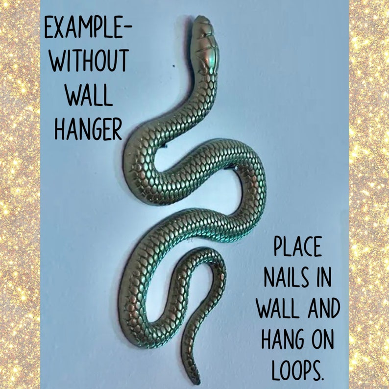 May include: A gold-colored snake sculpture with a textured surface. The sculpture is hanging from two loops. The text "EXAMPLE-WITHOUT WALL HANGER" is written above the sculpture. The text "PLACE NAILS IN WALL AND HANG ON LOOPS." is written below the sculpture.