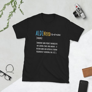 May include: Black t-shirt with white text that reads "ALDINERD/OL-DE-NARD/ (NOUN) SOMEONE WHO PRIDES THEMSELVES ON SAVING TIME AND MONEY. A PERSON WHO CAN OFTEN BE FOUND VIGOROUSLY SCOURING THE A.O.S."