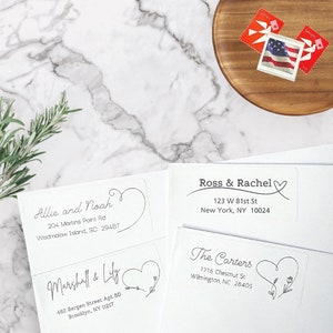 May include: Three white return address labels with black text and a heart design. The labels include the names Allie and Noah, Marshall and Lily, and Ross and Rachel, along with their respective addresses.