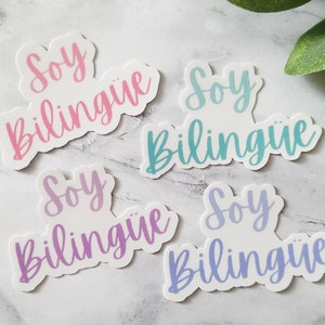 May include: Four white stickers with the phrase "Soy bilingüe" written in different pastel colors. The colors are pink, blue, purple, and light blue.